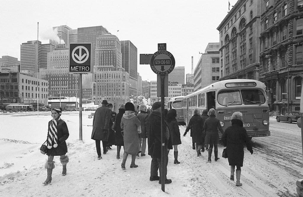 Winter street scene at Square Victoria with a Metro sign, bus, and pedestrians in snow