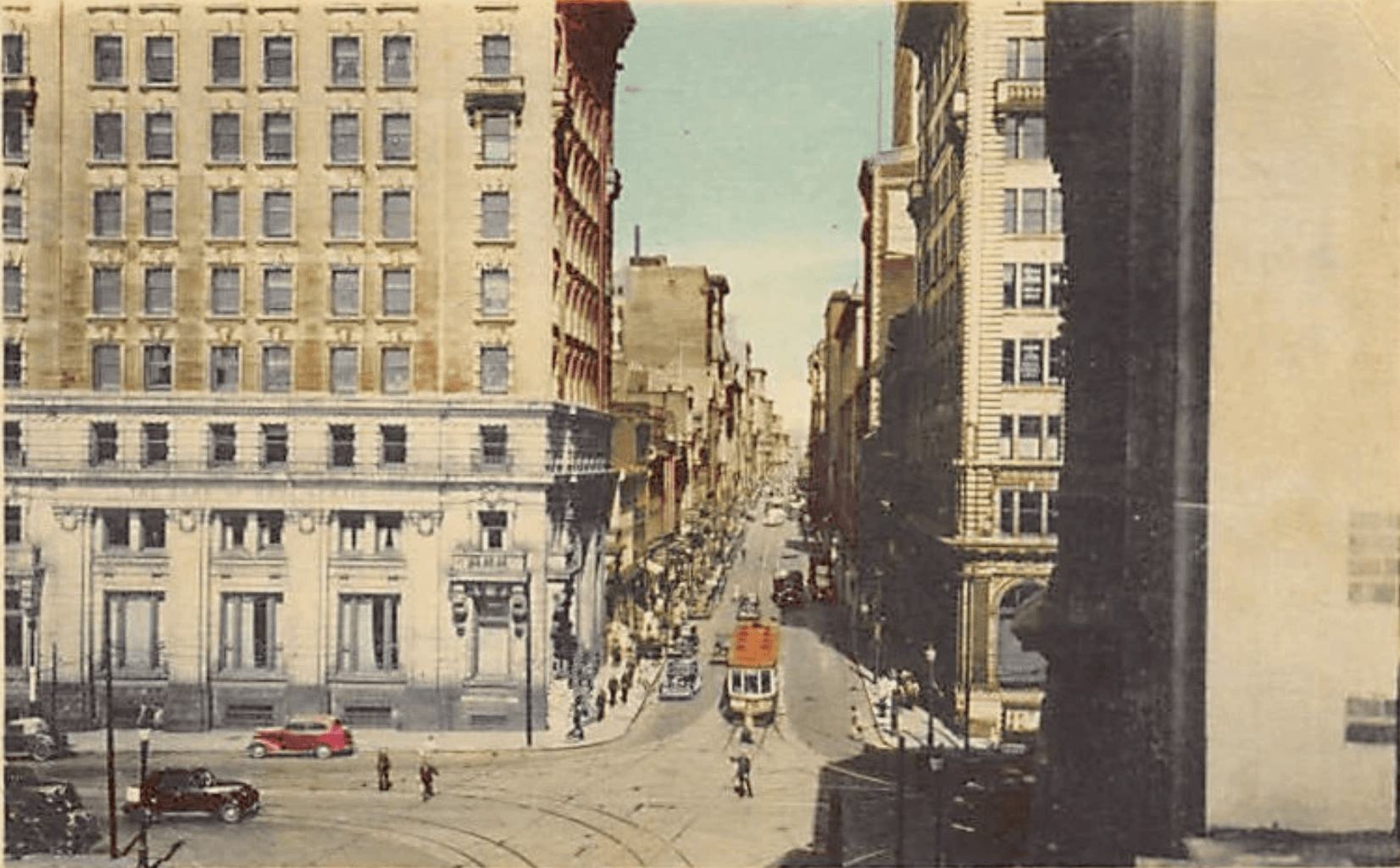 Hand-colored photograph of a street canyon with a vintage streetcar and early automobiles