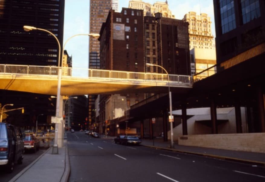 John Street in the Financial District in the 1970s, with a pedestrian overpass spanning a quiet street at dusk