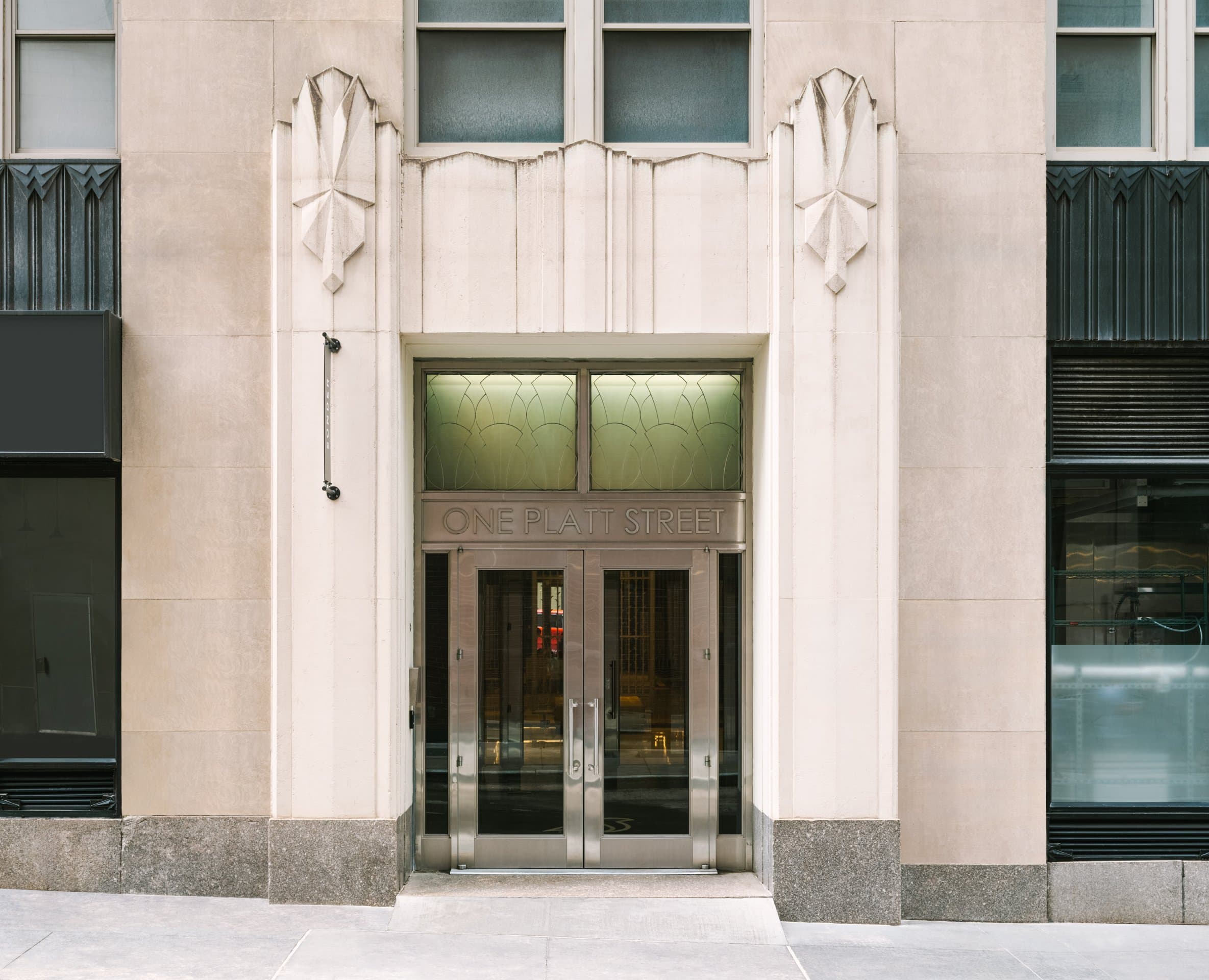 Art Deco limestone entrance of One Platt Street, with metal double doors under a One Platt Street transom