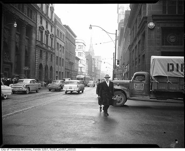 Archival photograph of King Street at Yonge in the 1950s, with cars, a delivery truck, and a man walking in the street